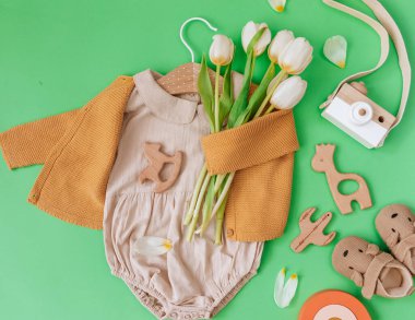 Düz Yerde Yeni Doğan Moda Arkaplanı. Moda, bebek kıyafetleri ve yeşil arka planda laleleri olan bir oyuncak. Blogcular için Yaz Bebeği Moda Konsepti. 