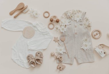 Bebek ve yeni doğanlar için kıyafetler: beyaz tulumlar ve aksesuarlar nötr bej ve kahverengi renkler. Çevre dostu ahşap oyuncaklar arka planda, üst tarafta, düz yerde.