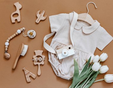 Laleli ve tahta oyuncaklı şirin bir bebek vücudu vardı. Kahverengi arka planda çocuk kıyafetleri ve aksesuarları. Yeni doğan moda.. 