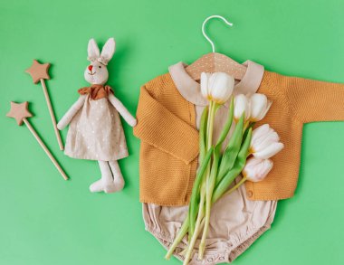 Düz Yerde Yeni Doğan Moda Arkaplanı. Moda, bebek kıyafetleri ve yeşil arka planda laleleri olan bir oyuncak. Blogcular için Yaz Bebeği Moda Konsepti. 