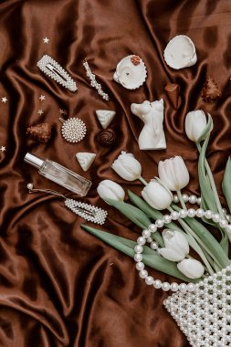 Beyaz laleler, inci çanta, parfüm şişesi, kadın aksesuarları ve kahverengi ipek arka planda bijouterie ile düz bir moda kompozisyonu. yaşam tarzı konsepti.