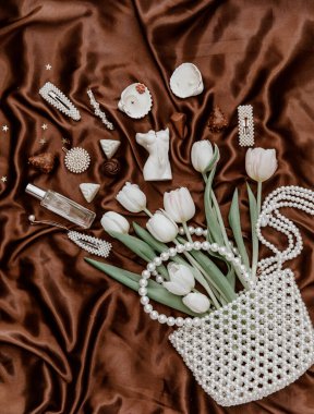 Beyaz laleler, inci çanta, parfüm şişesi, kadın aksesuarları ve kahverengi ipek arka planda bijouterie ile düz bir moda kompozisyonu. yaşam tarzı konsepti.