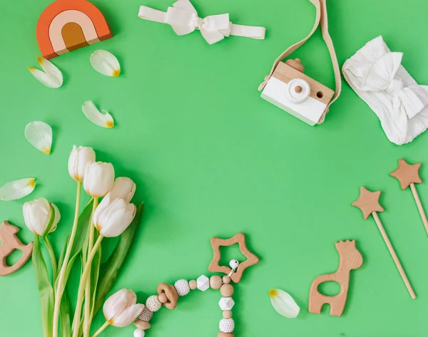 Set of baby items and accessories on green background. Wooden toys and tulips flat lay. Blogger background
