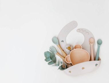 Bebek beslenme aksesuarları. Silikon önlük, bulaşık takımı. Düz konum, üst görünüm, kopyalama alanı.