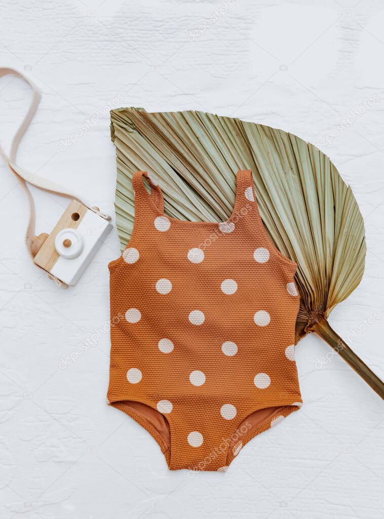 Still life baby summer concept. Vintage baby swimsuit, wooden camera toy and  with palm leaf on white background. Summer concept for kids, Top view, flat lay, copy space 