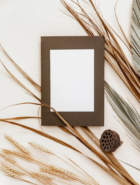 Boş tebrik kartı maketi, bej masa arkasında kuru palmiye yaprağı. İskandinav tarzında bir düğün şablonu. Durgun bir hayat.