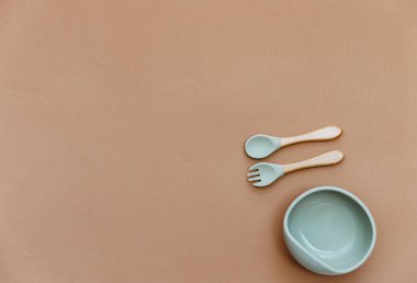 Bebek maması aksesuarlı kompozisyon. Kahverengi arka planda silikon kase ve kaşık. Tarafsız pastel renkler 
