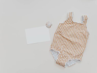 Summer kid's vacation concept - swimsuit with blank card and seashells on neutral background, minimal holiday  fashion baby 