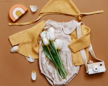 Beyaz arka planda yazlık bebek kıyafetleri, yeni doğan moda konsepti laleli tarafsız vücut giysisi ve çevre dostu oyuncaklar. Üst görünüm 