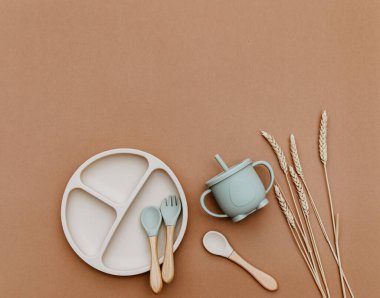 Masada parlak bebek bulaşık takımları, modaya uygun kahverengi arka planda silikon setleri, düz yatış. Bebek maması servisi..