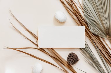 Boş tebrik kartı maketi, kuru palmiye yaprağı ve bej masa zemininde mumlar. Asgari markalaşma, İskandinav tarzında düğün şablonu. 