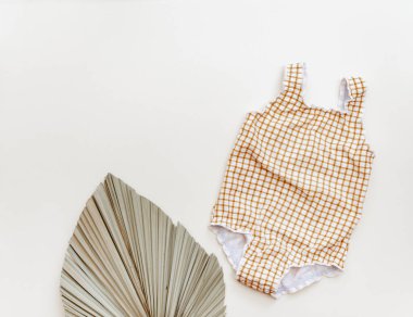 Bej arka planda palmiye yaprağı olan bebek mayosu, yaz tatili konsepti çok az. Düz yatış, üst görünüm