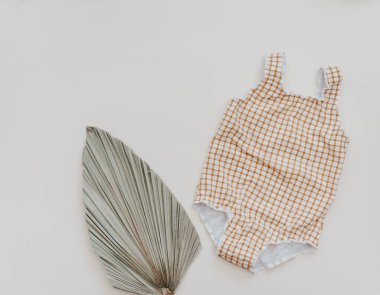 Yaz çocuğunun tatil konsepti. Tarafsız arka planda palmiye yaprağı olan mayo, moda bebeği. 