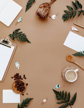 Kahverengi, nötr çalışma masası, kahve ve ofis malzemeleri. El işi defteri, yeşil zeytin yaprağı ve malzemelerle dolu düz bir çalışma masası. Ev blogçusu