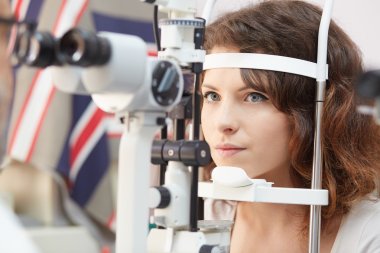 Güzel kadın göz laboratuarında bir konsantrasyon ile göz testi makineye arıyor