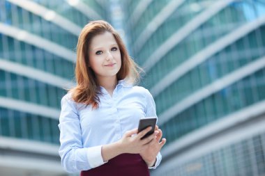 Ofis binaları arka planda, sokakta cep telefonuyla çalışan bir yönetici.