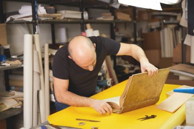 Kitap klasörü el sanatları atölyesindeki eski kitabı yeniliyor