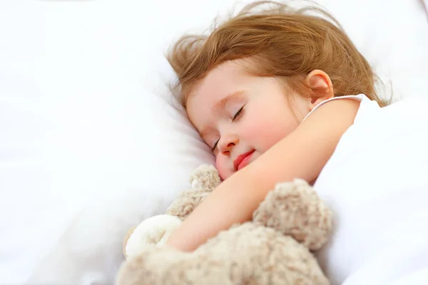 Criança menina dorme na cama com ursinho de pelúcia — Fotografia de Stock