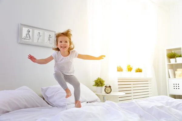 Happy child girl jumps and plays bed — Stock Photo, Image