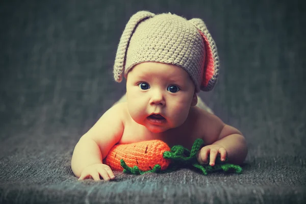 Bambino felice in costume un coniglietto con carota su un grigio — Foto Stock