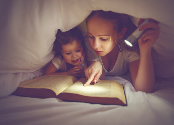 Family reading bedtime. Mom and child reading book with a flashl