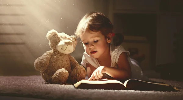 Criança menina lendo um livro de magia em casa escura — Fotografia de Stock