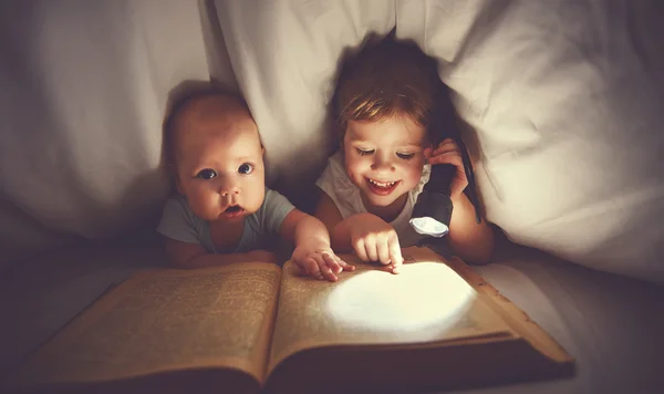 子供たちの兄と妹が b の下 aflashlight と本を読んでください。 — ストック写真