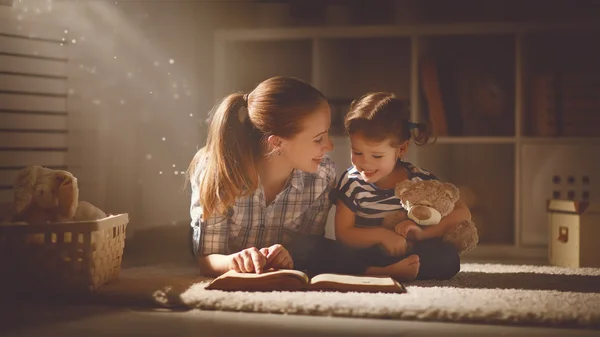 Gelukkige familie moeder en dochter lezen een boek in de avond — Stockfoto