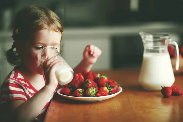 Feliz niña bebe leche y come fresas en verano hom —  Fotos de Stock