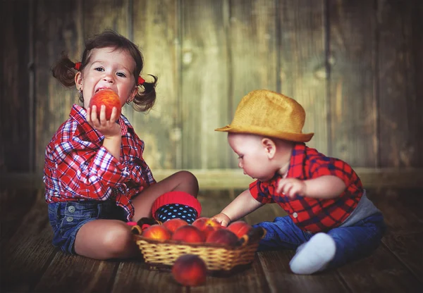 Счастливые дети сестра и младший брат с корзиной персиков — стоковое фото