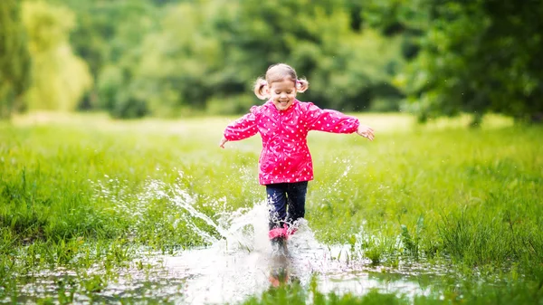 Happy child girl running and jumping in puddles after rain — Stock Photo, Image