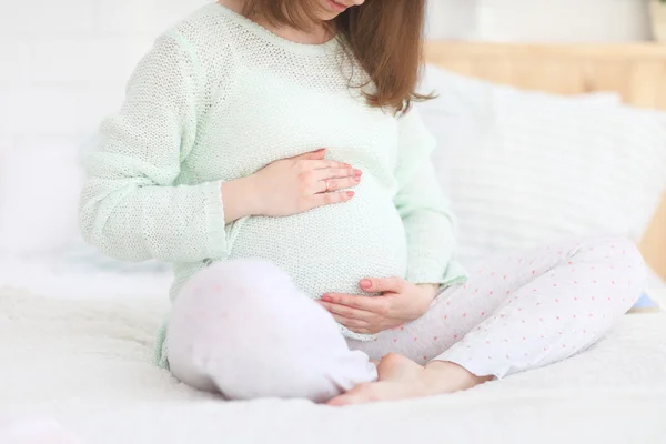 Pancia di una donna incinta seduta su un letto — Foto Stock