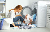 Mutter Hausfrau mit Baby faltet Kleidung in die Waschmaschine