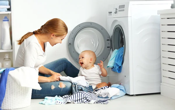 Mutter Hausfrau mit Baby faltet Kleidung in die Waschmaschine — Stockfoto