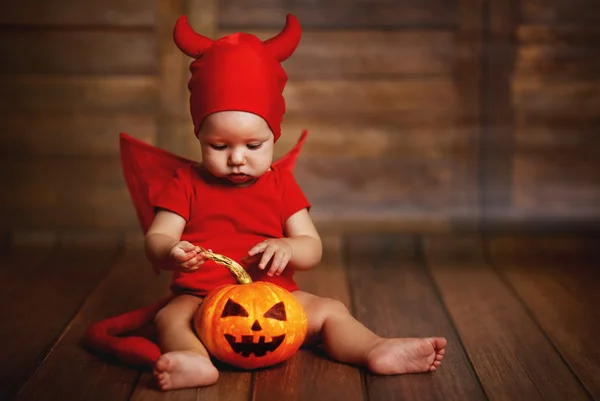 funny baby in devil halloween costume with pumpkin