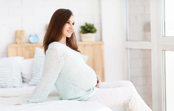 Pregnant woman sitting on a bed — Stock Photo, Image