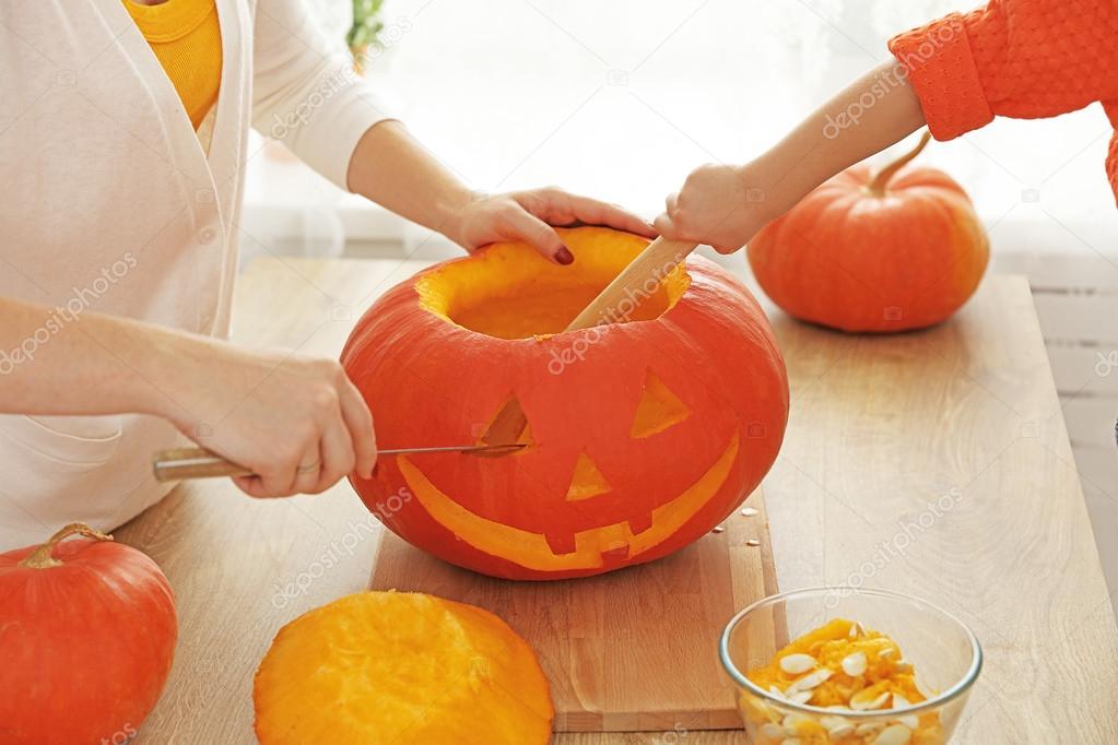 Hands of family mother and child cut pumpkin for Halloween