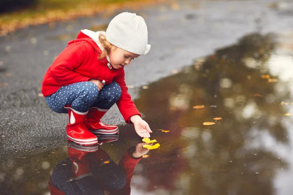 Felice bambina che gioca con le foglie autunnali in una pozzanghera dopo un — Foto Stock