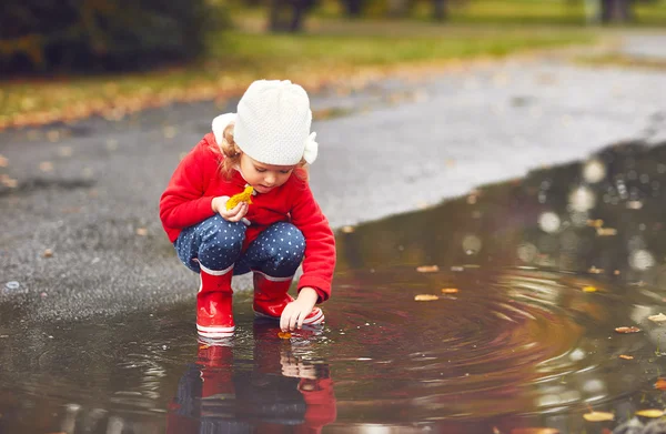 Felice bambina che gioca con le foglie autunnali in una pozzanghera dopo un — Foto Stock