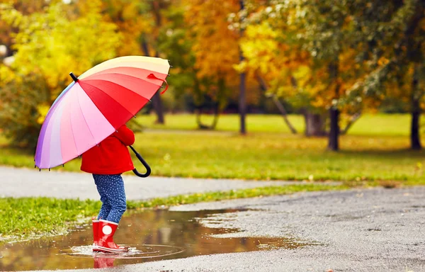 Счастливая девочка с зонтиком, идущая через лужи за аутом — стоковое фото