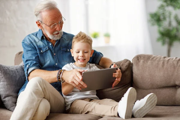 幸せな家族高齢者の祖父と少年はソファに座って 週末にタブレットで漫画を見ます家で一緒に — ストック写真
