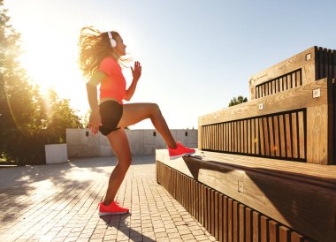 Spor giyim ve kulaklıklı sağlıklı, aktif genç bir bayanın yaz mevsiminde merdivenlerin yanında yoğun koşu egzersizi yaparken tüm vücudu görüyordu.
