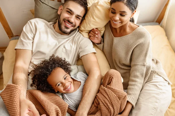 Mutlu aile çok ırklı anne, baba ve oğul gülüyor, oynuyor ve yatak odasında gıdıklanıyor.