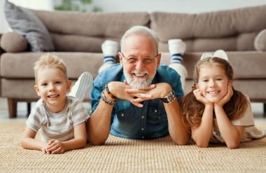 Mutlu aile: mutlu kıdemli adam gülümseyen ve kameraya bakan hafta sonu evde torun ve torununun yanında yatarken.