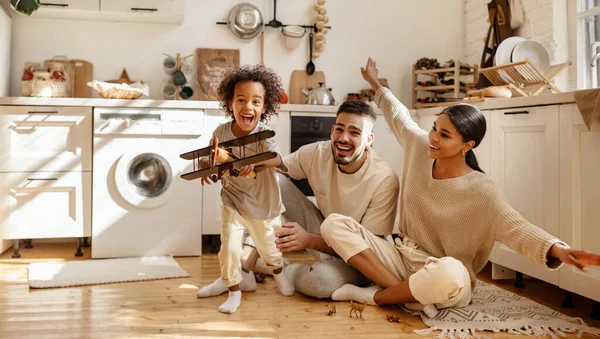快乐的多民族家庭 小男孩在厨房里当着父母的面笑着玩玩具飞机 — 图库照片