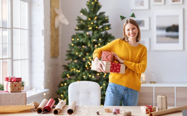 幸せな若い女性のための贈り物クリスマス休暇の笑顔カメラで自宅 — ストック写真