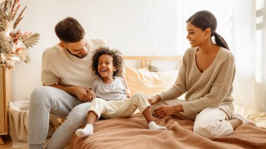 Mutlu aile çok ırklı anne, baba ve oğul gülüyor, oynuyor ve yatak odasında gıdıklanıyor.