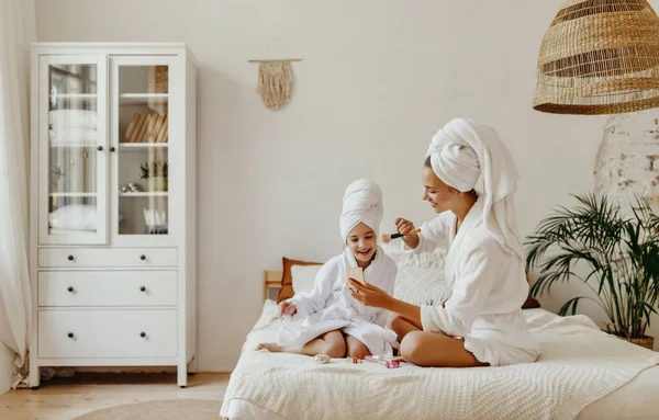 happy family mother and little daughter in dressing gowns and towels laugh and do makeup  a Spa day at hom