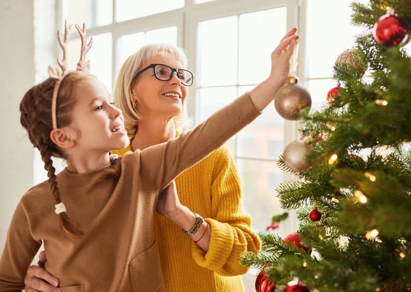 愛らしい子供と笑顔の祖母は冬の休日のための黄金の泡でクリスマスツリーを飾る — ストック写真