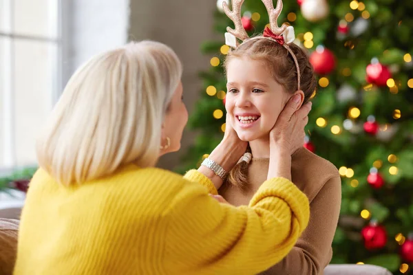 喜びの祖母は幸せな孫娘を愛撫しながら クリスマスツリーと一緒に部屋に座って それぞれを見て — ストック写真